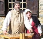 photo of John and Jan Haigis standing outside by a split-rail fence on a sunny day, wearing pioneer costumes
