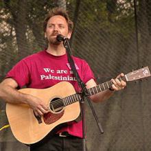 photo of David Rovics singing and playing guitar in concert