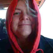 photo of Kiya Heartwood peering out from within a red hooded sweatshirt